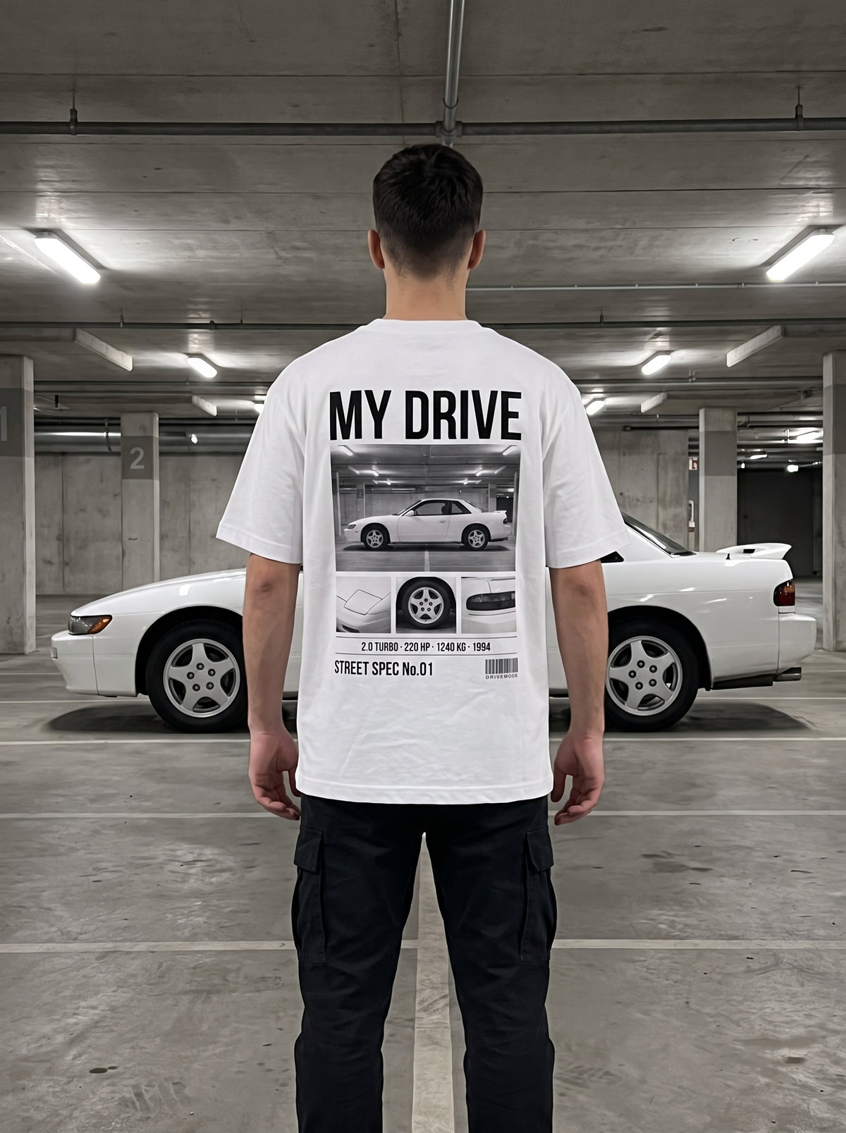T-shirt personnalisé DriveMode blanc oversize porté de dos devant la voiture imprimée au dos, dans un parking souterrain