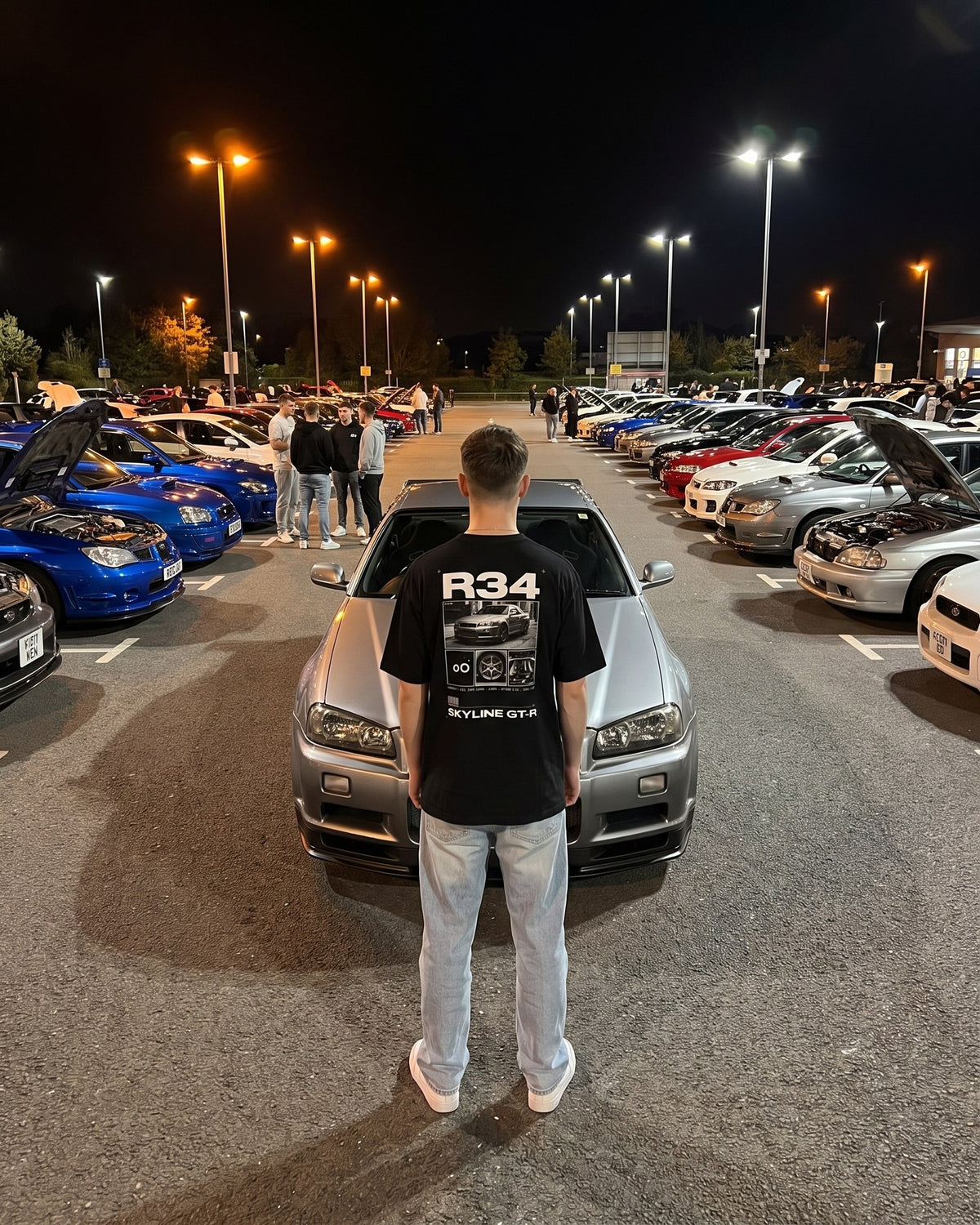 T-shirt oversize R34 porté de dos devant une Skyline R34 lors d'un meet de nuit