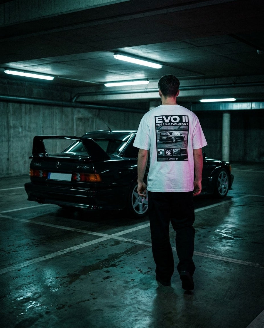 T-shirt Evo II blanc porté de dos dans un parking souterrain devant une Mercedes 190E Evo II noire